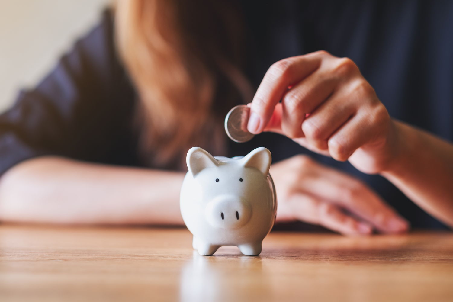 Eine Frau wirft Geld in ein Sparschwein.