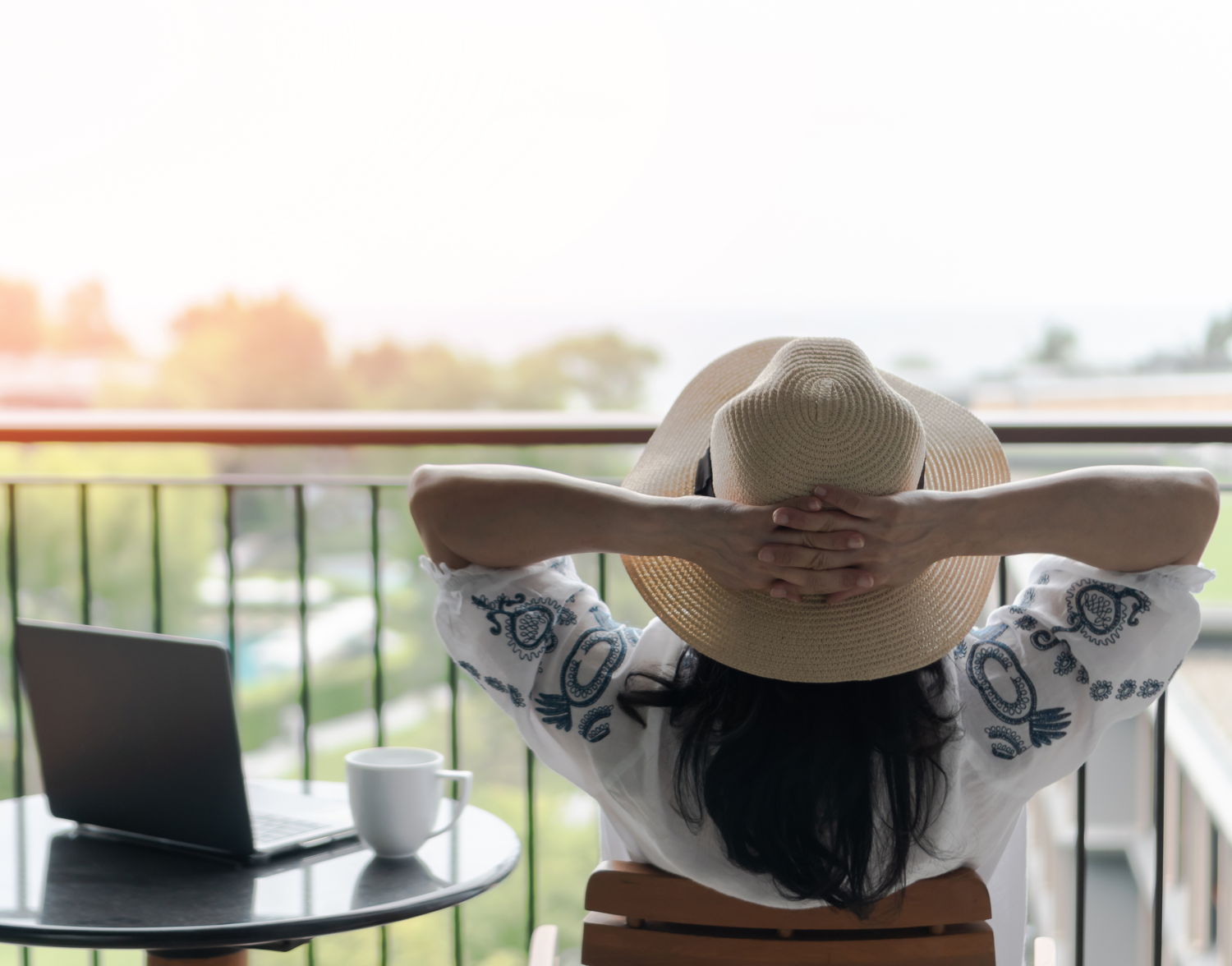 Eine Frau sitzt neben Ihrem Laptop auf einem Balkon und entspannt.
